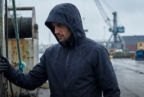 Handwerker in gelber Regenjacke und Regenhose bei Regen auf der Baustelle